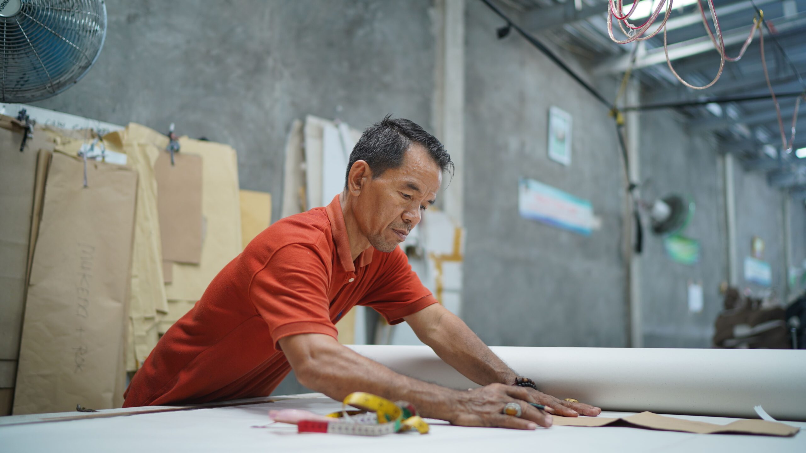 pexels ibnu lantib 46443009 32258042 Senior craftsman measuring fabric patterns at wooden workbench in industrial workshop, custom tailoring focus